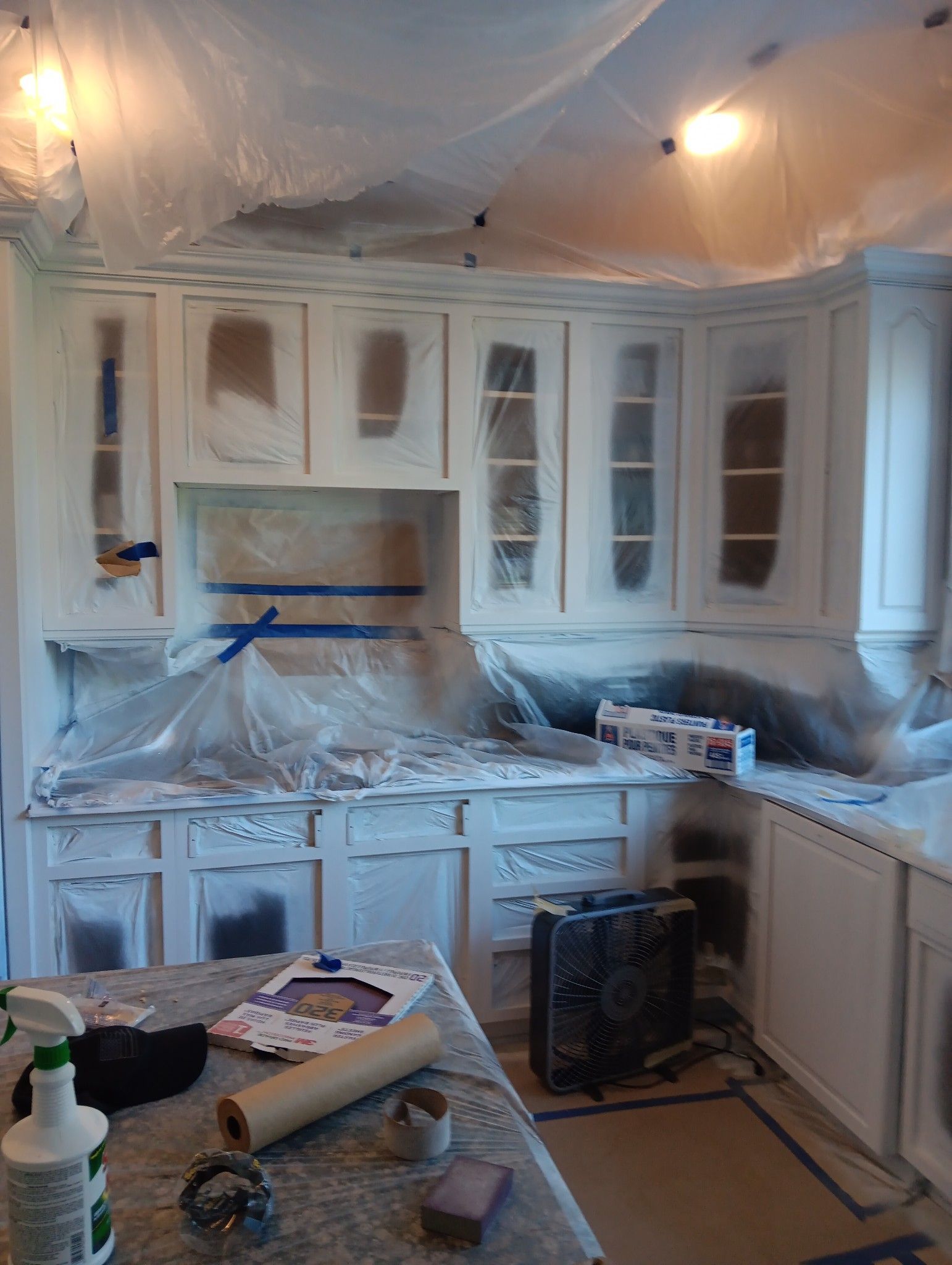 A kitchen is being painted with white cabinets and granite counter tops.