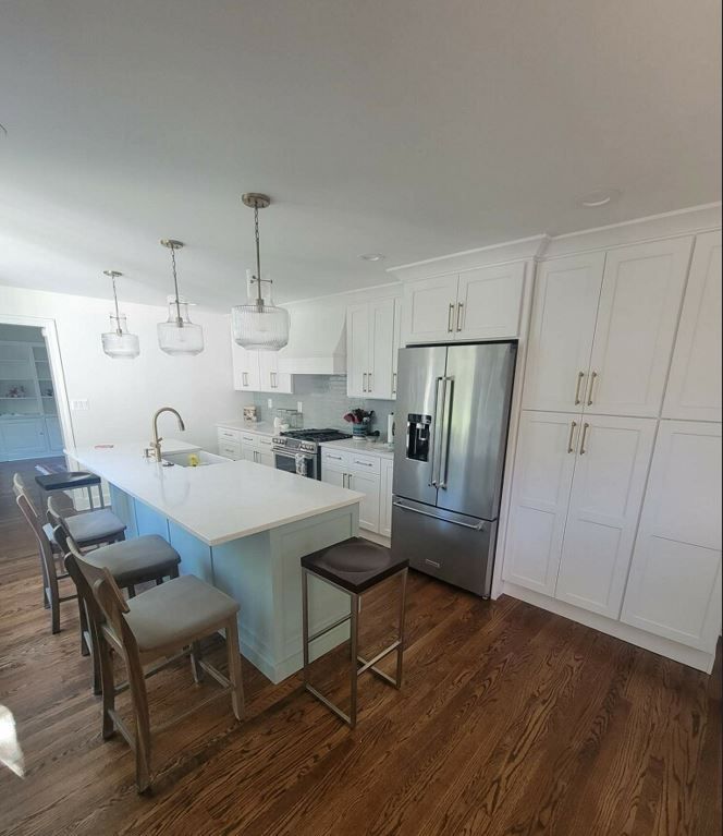 A kitchen with white cabinets , stainless steel appliances , hardwood floors and a large island.