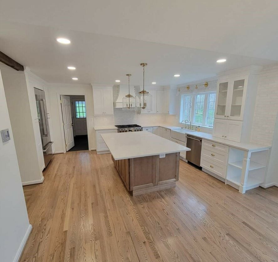 A kitchen with hardwood floors and white cabinets has a large island in the middle.