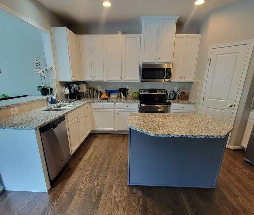 A kitchen with white cabinets , granite counter tops , stainless steel appliances and a large island.