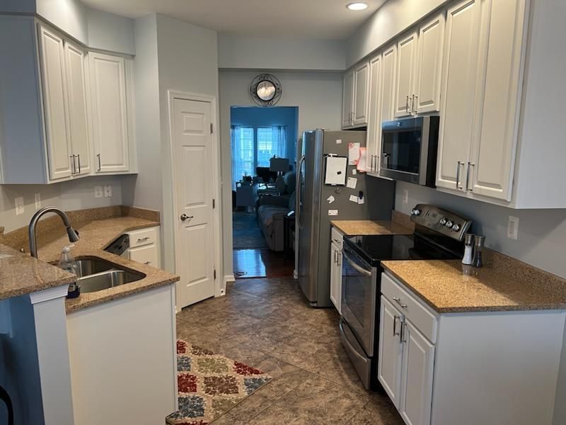 A kitchen with white cabinets , stainless steel appliances , granite counter tops and a sink.