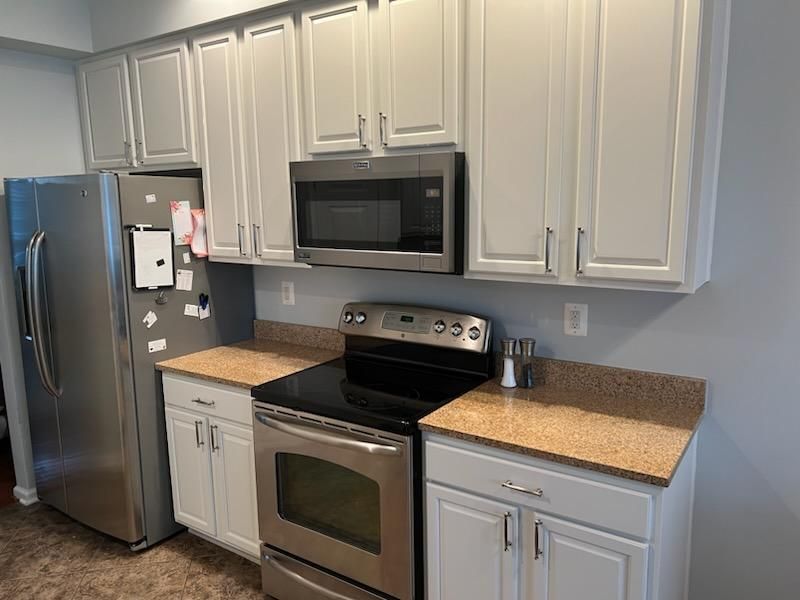 A kitchen with stainless steel appliances , white cabinets , granite counter tops , and a refrigerator.