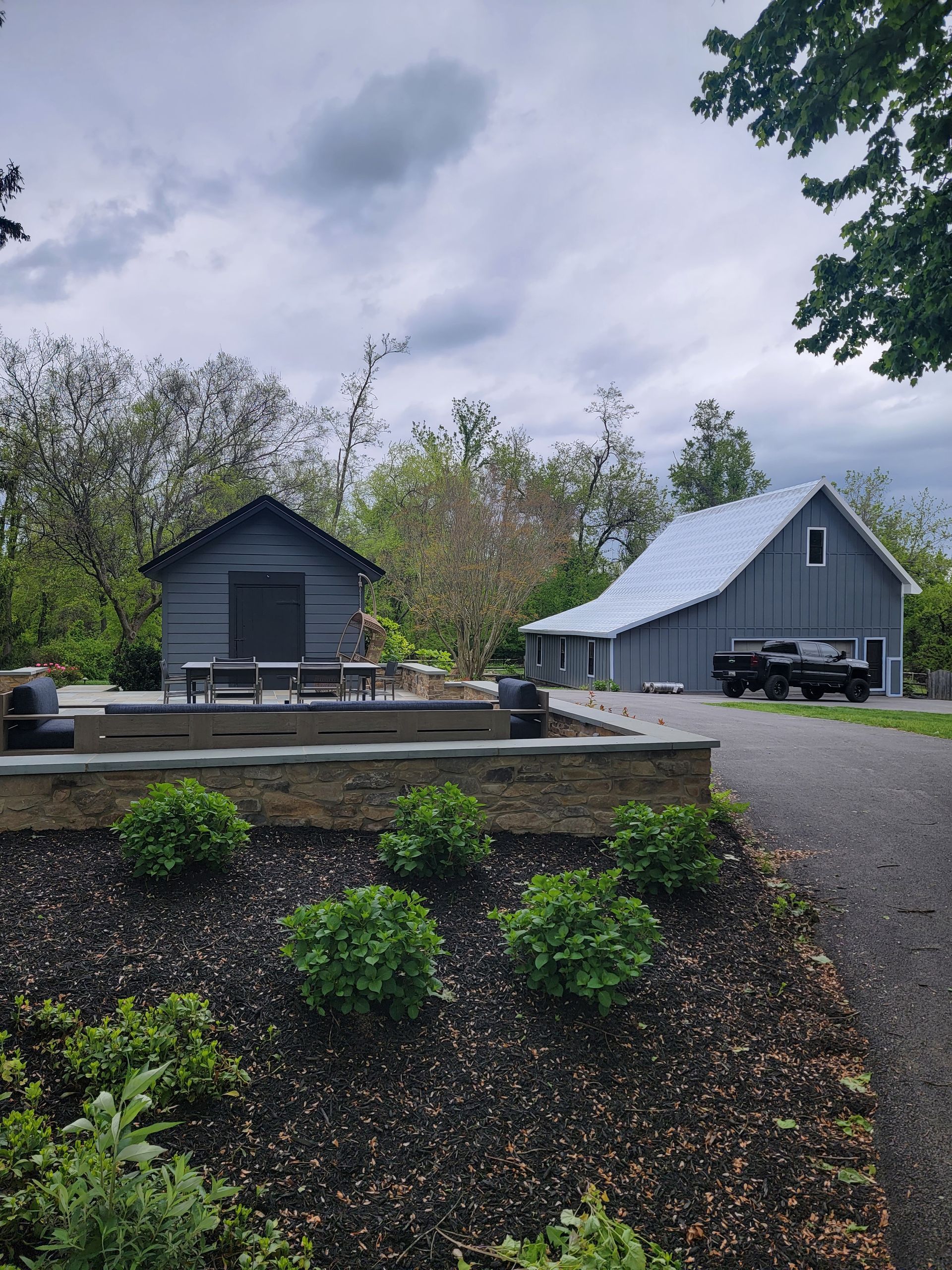 A gray barn with a blue roof is next to a smaller barn