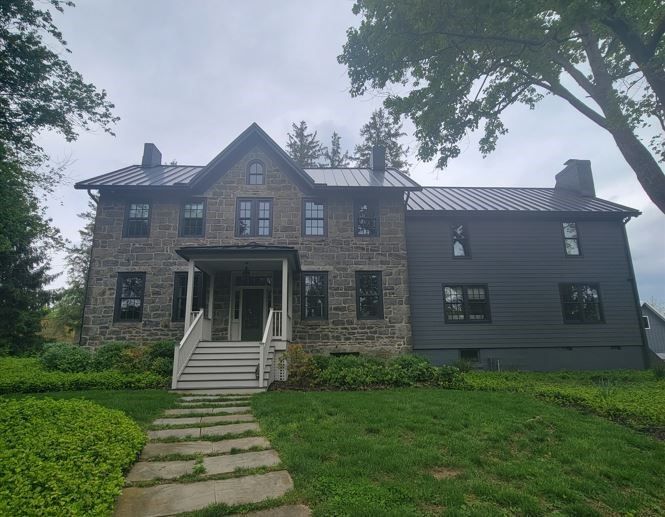 A large stone house with a metal roof is sitting on top of a lush green hill.