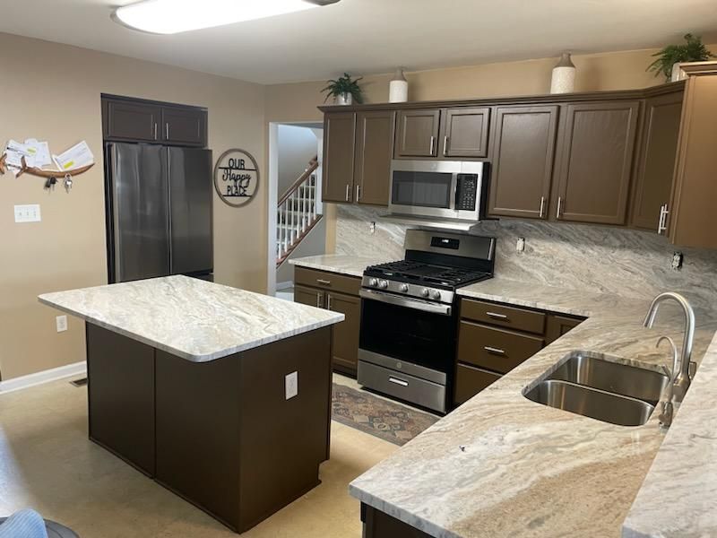 A kitchen with brown cabinets , stainless steel appliances , granite counter tops and a large island.
