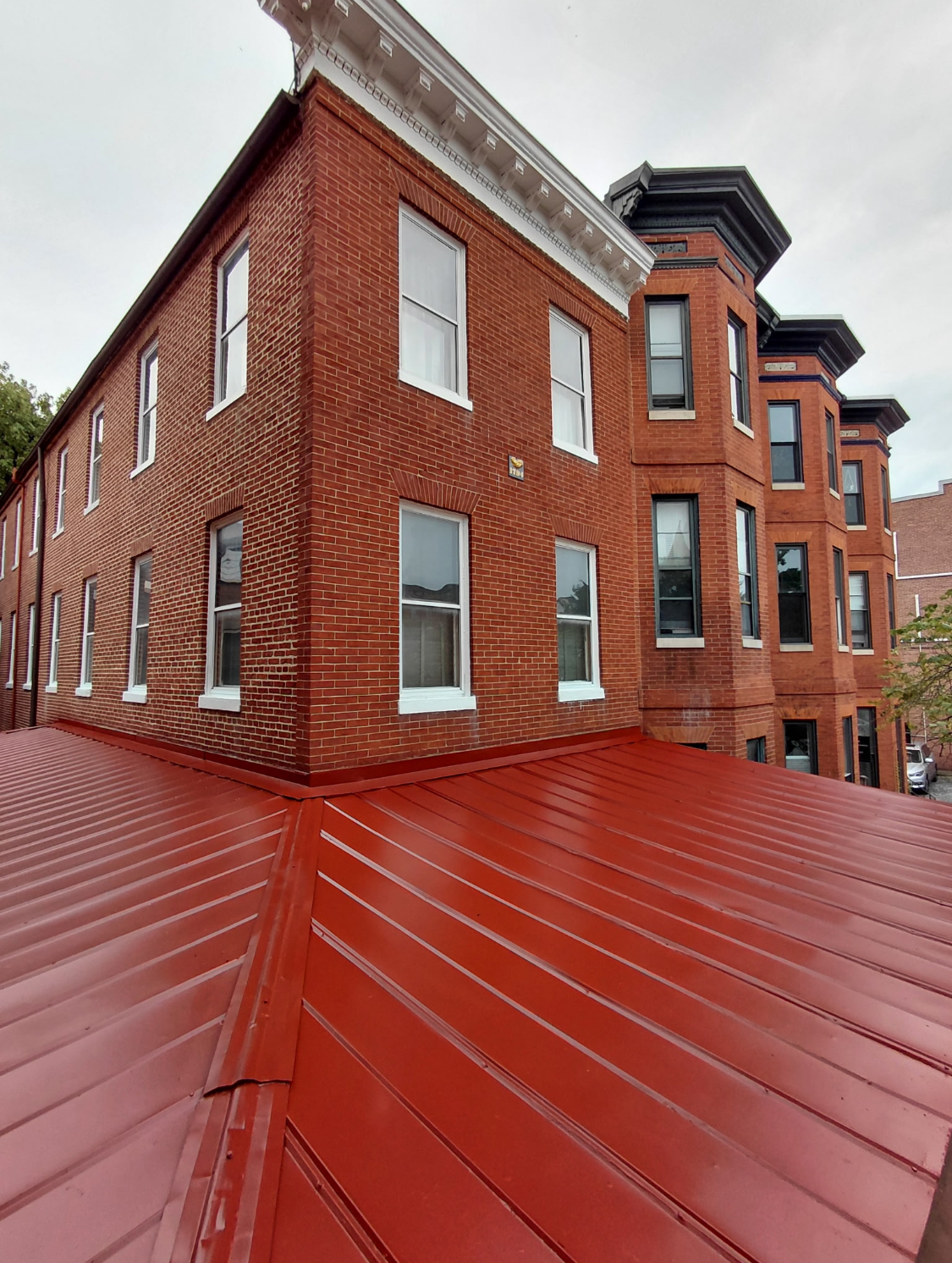 Red metal roof on a brick building corner. Other brick buildings in the background. 