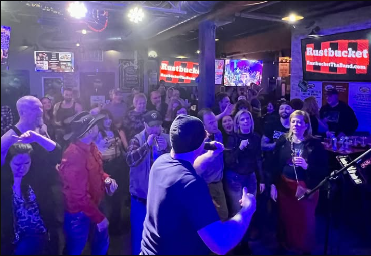 Crowded bar with a live band performing under purple lights and a cheering audience