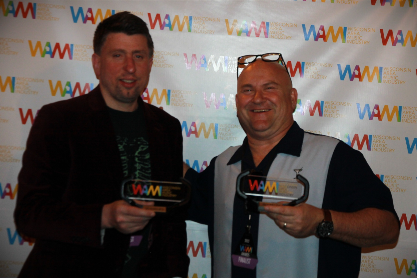 Two people holding WAW plaques at an event backdrop, smiling at the camera.