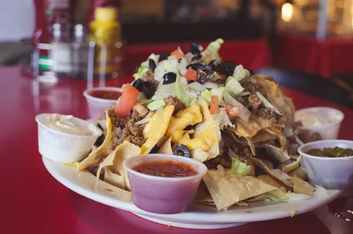 Nachos piled high with toppings, served with side dips on a red table.