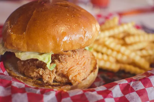 Chicken sandwich with lettuce on a bun, alongside a serving of crinkle-cut fries, in a red and white checkered basket.