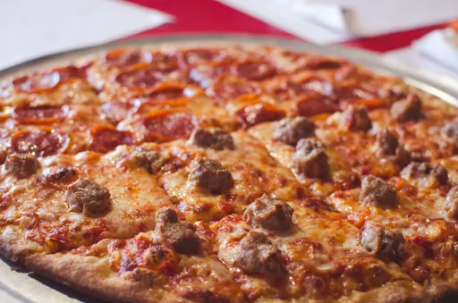 Pizza, half pepperoni, half sausage, on a metal tray, red background.