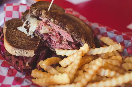 Reuben sandwich on rye bread with crinkle-cut fries in a red and white checkered basket.