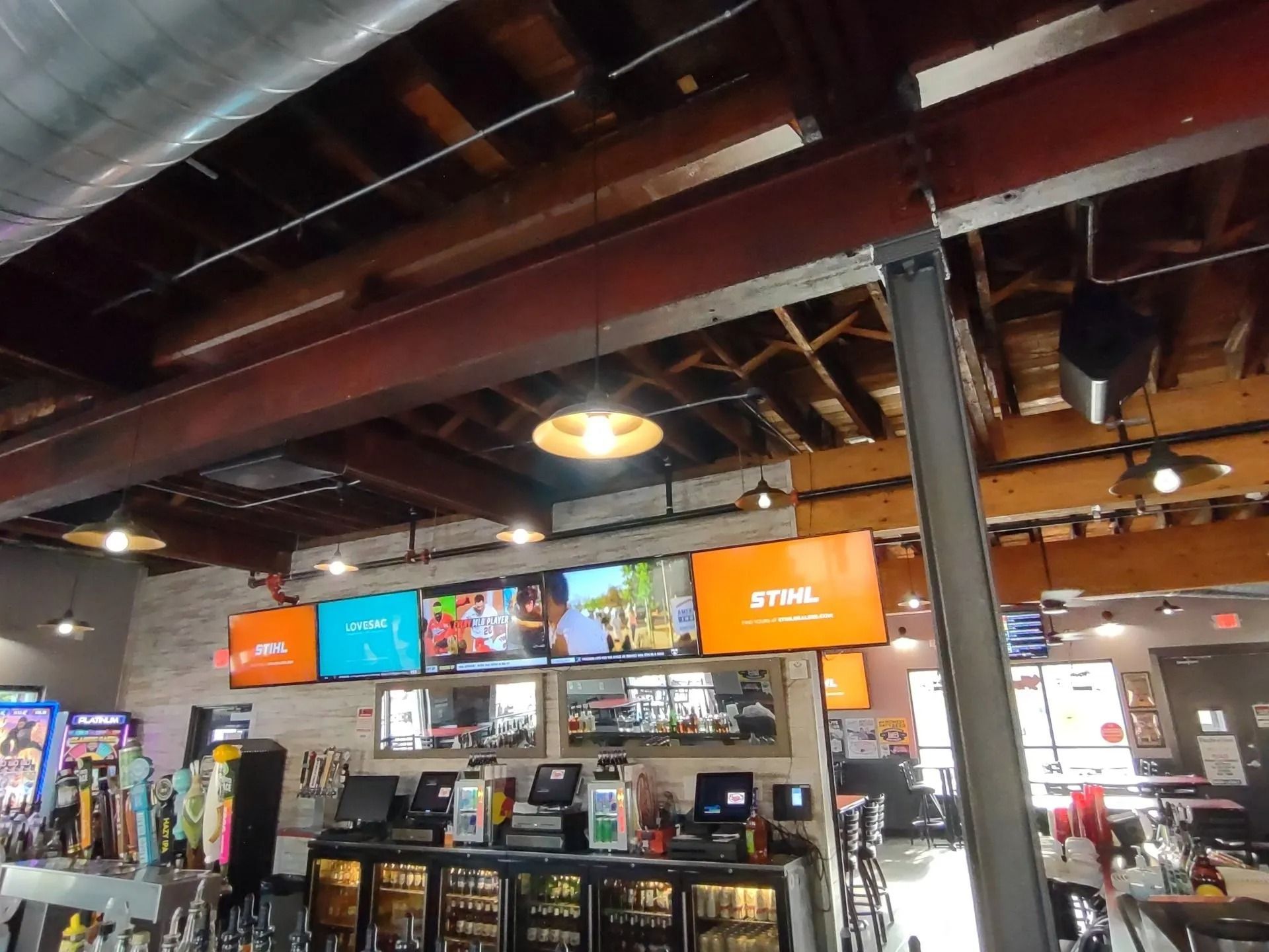 Coffee shop interior with exposed beams, hanging lights, and menu screens above the counter