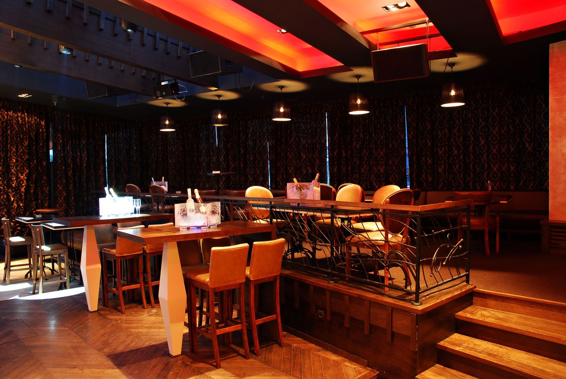 Empty modern bar and lounge with warm orange lighting, wooden tables, and stools on a raised platform