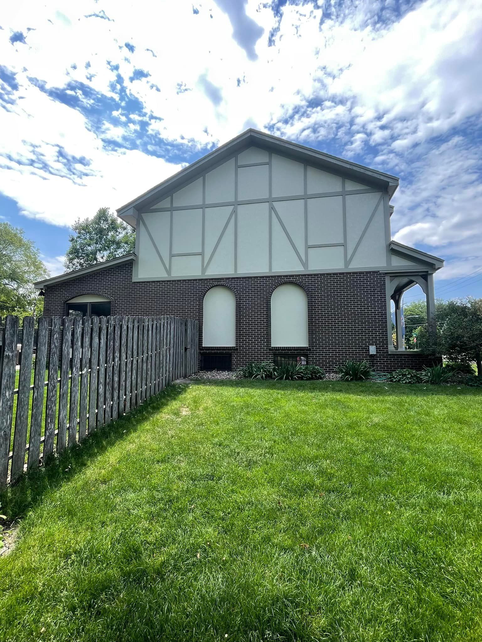 Log cabin with a painted upper section and a green lawn under a blue, cloudy sky.