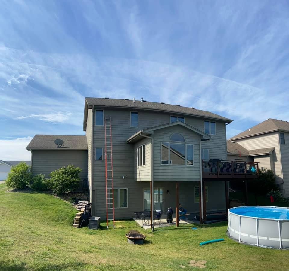 Backyard view of a two-story beige house with an attached deck, above-ground pool, and a ladder leaning against the siding.