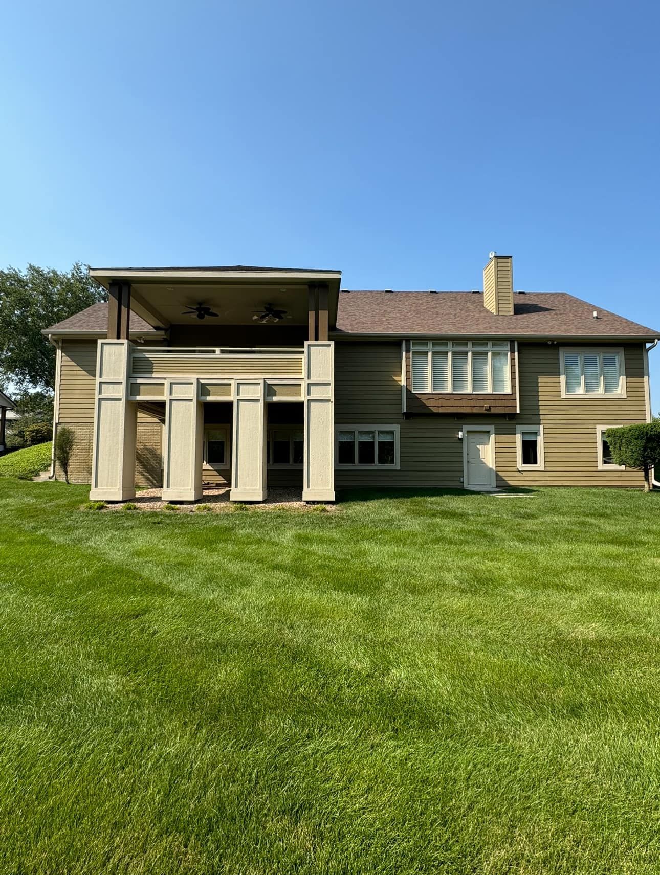 Back view of a light brown house with a green lawn and clear blue sky.