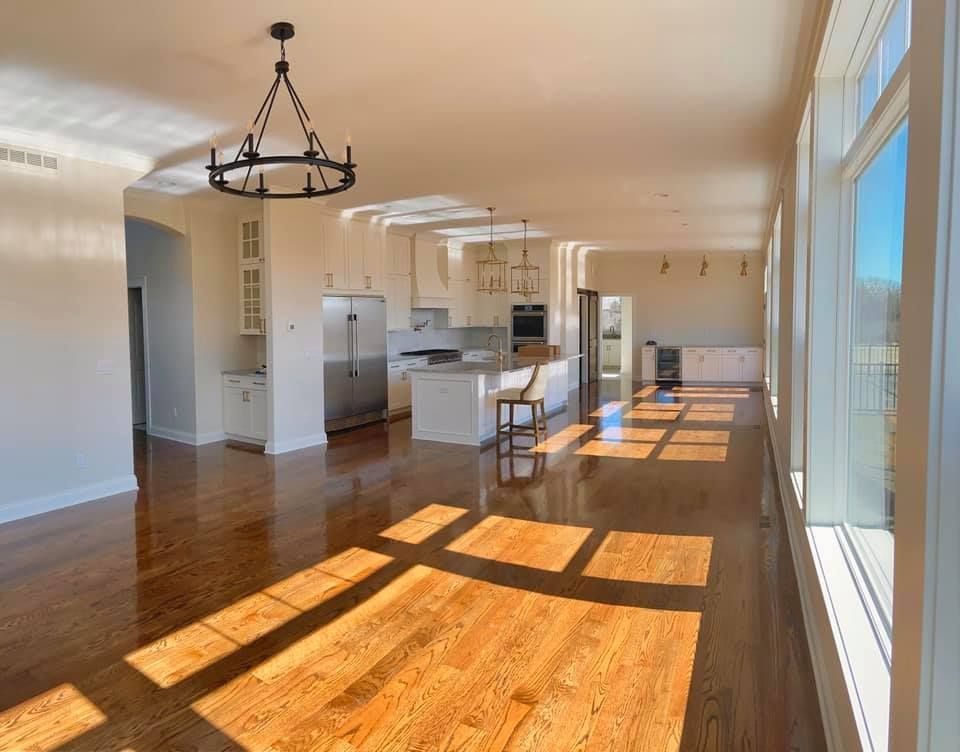 Spacious sunlit kitchen with wood floors, white cabinets, and stainless steel appliances.