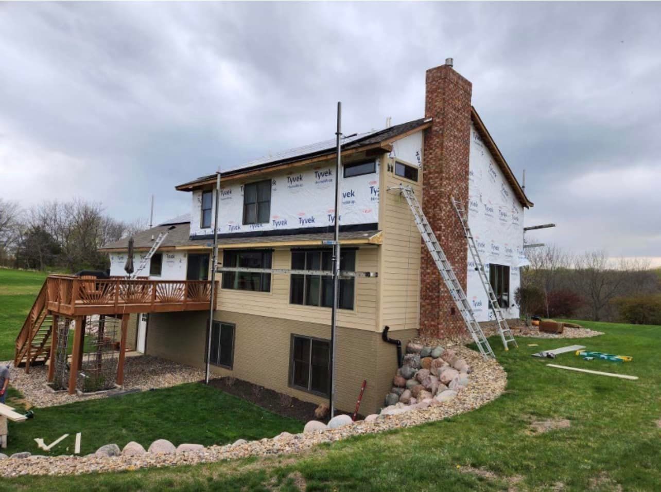 House under construction; siding installation in progress. Yellow and brown siding with brick chimney.