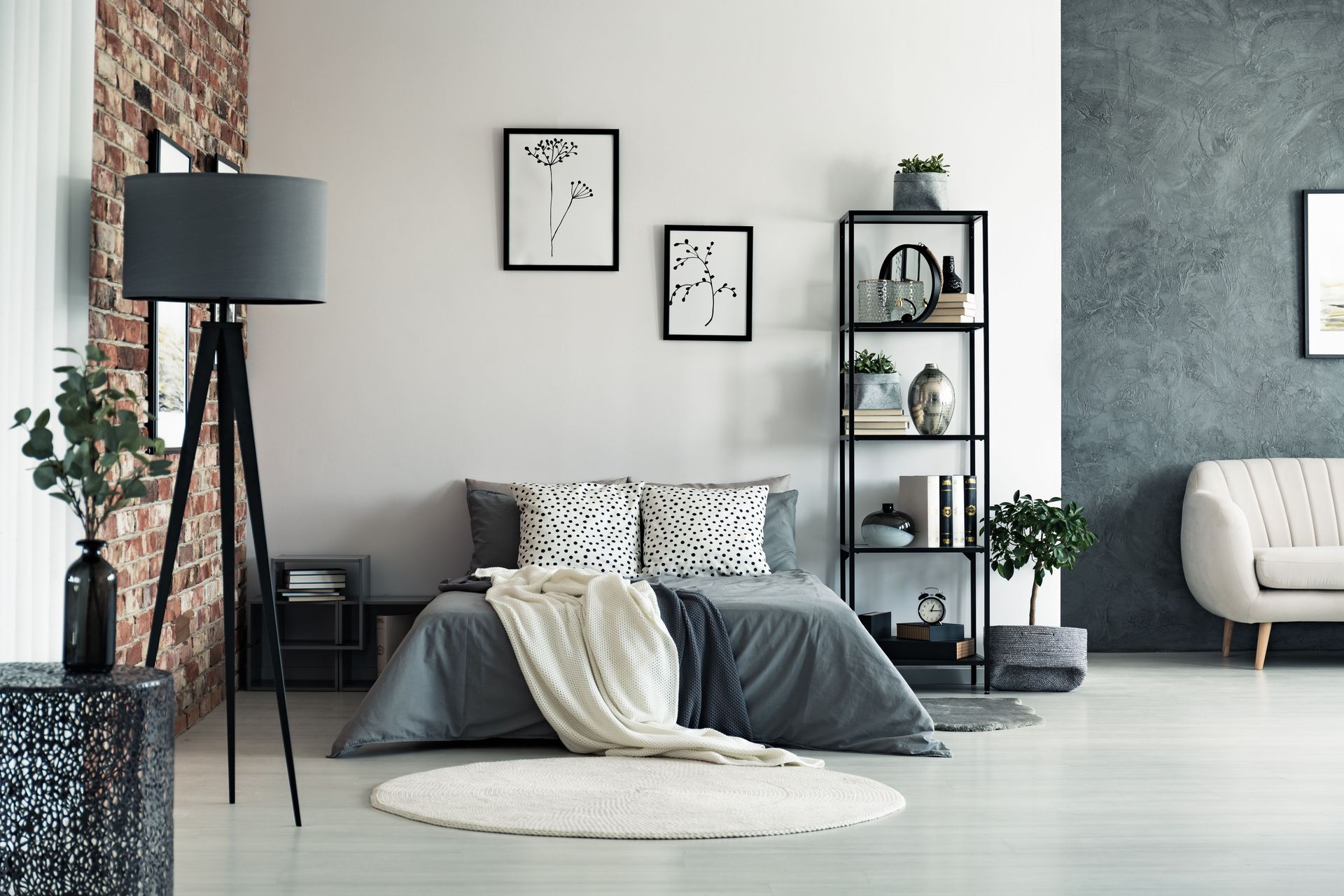 Bedroom with gray bed, brick wall, lamp, shelf, and white rug.