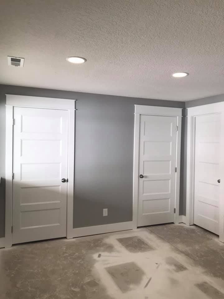 Interior view of a room with three white paneled doors and grey walls. Recessed lighting.