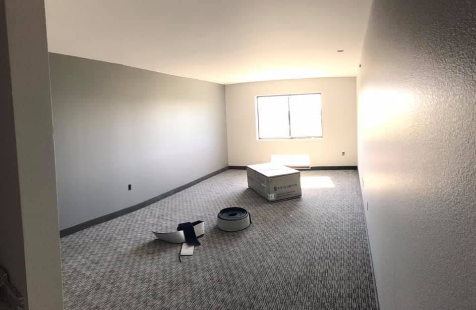 Empty room with gray walls, carpet, and a closed window, containing a box and debris.