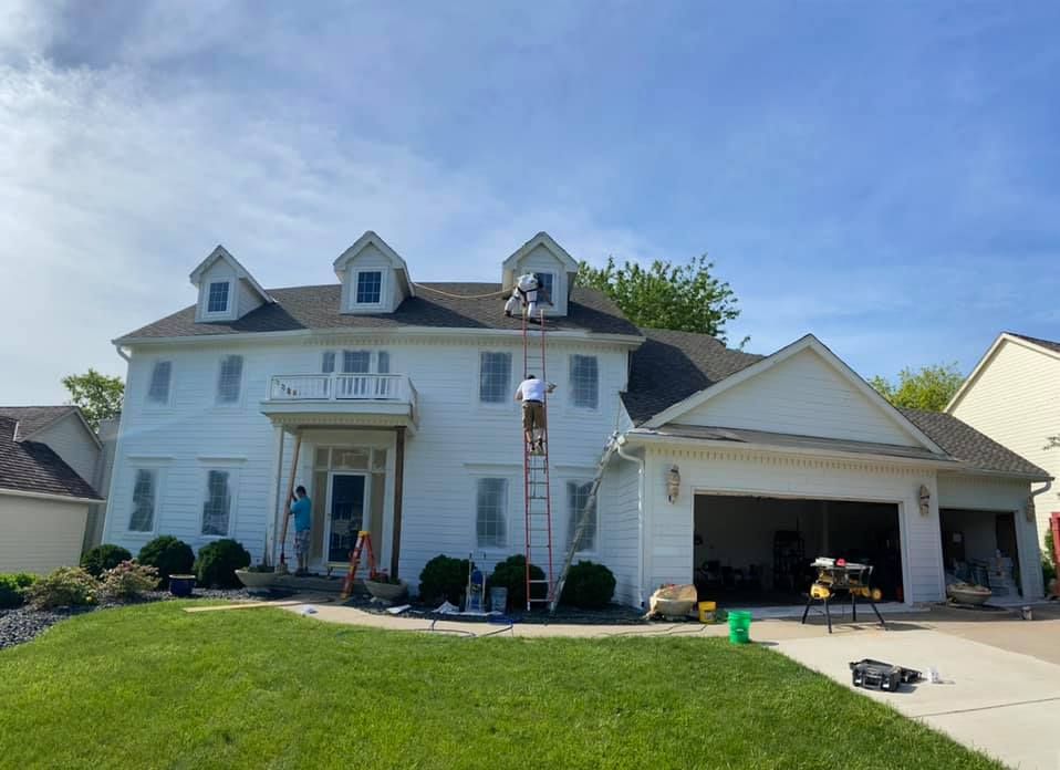 House being painted by three people on ladders on a sunny day.