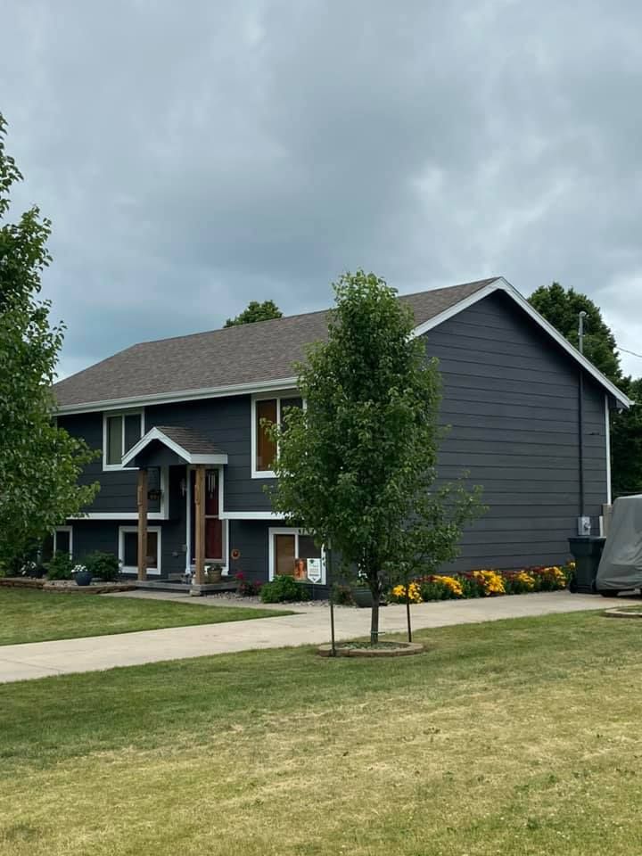 Two-story house with dark gray siding, white trim, and brown roof under a cloudy sky.