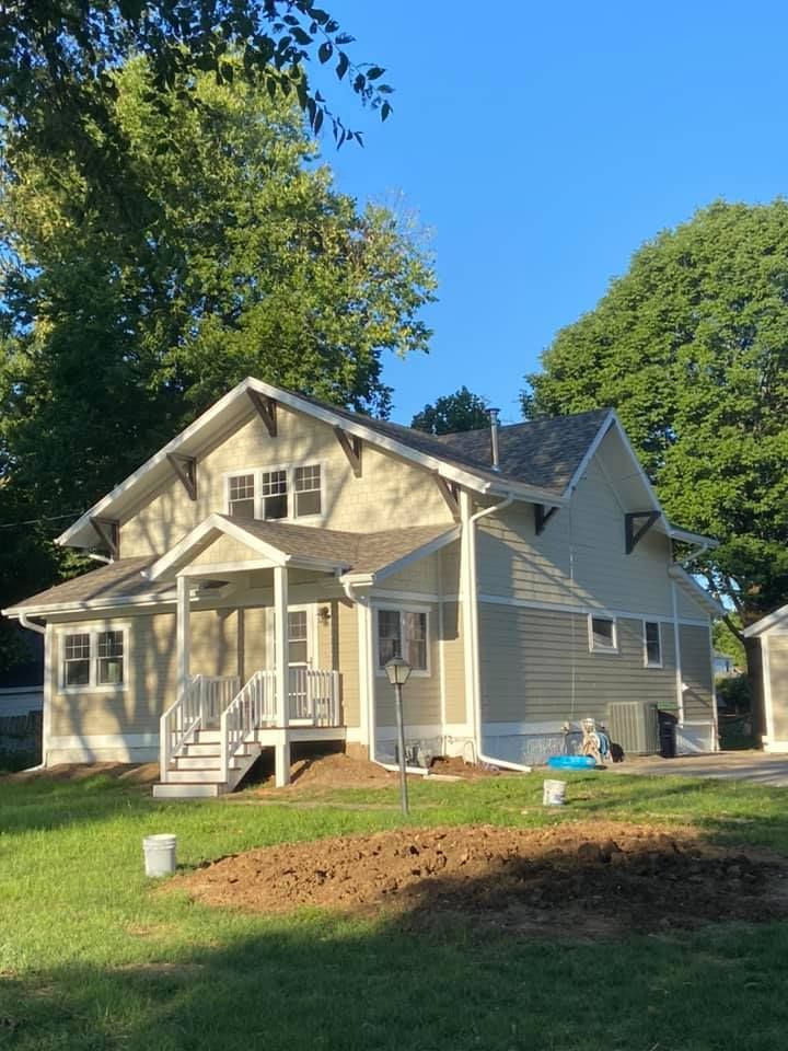 Two-story house with light green siding and white trim, front porch, and grassy yard.