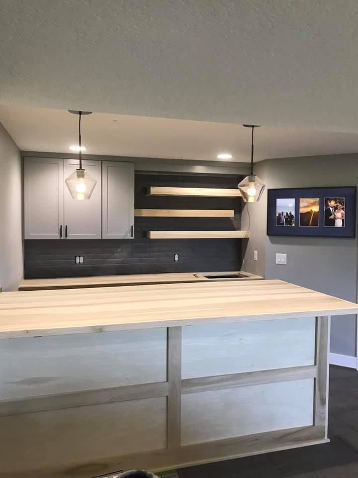 Kitchen island and cabinets with light wood counter and gray cabinets. Open shelving and pendant lights.