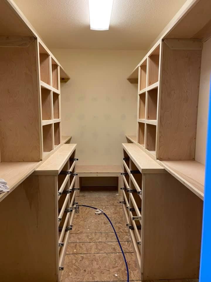 Walk-in closet with built-in shelves and drawers; light wood finish.