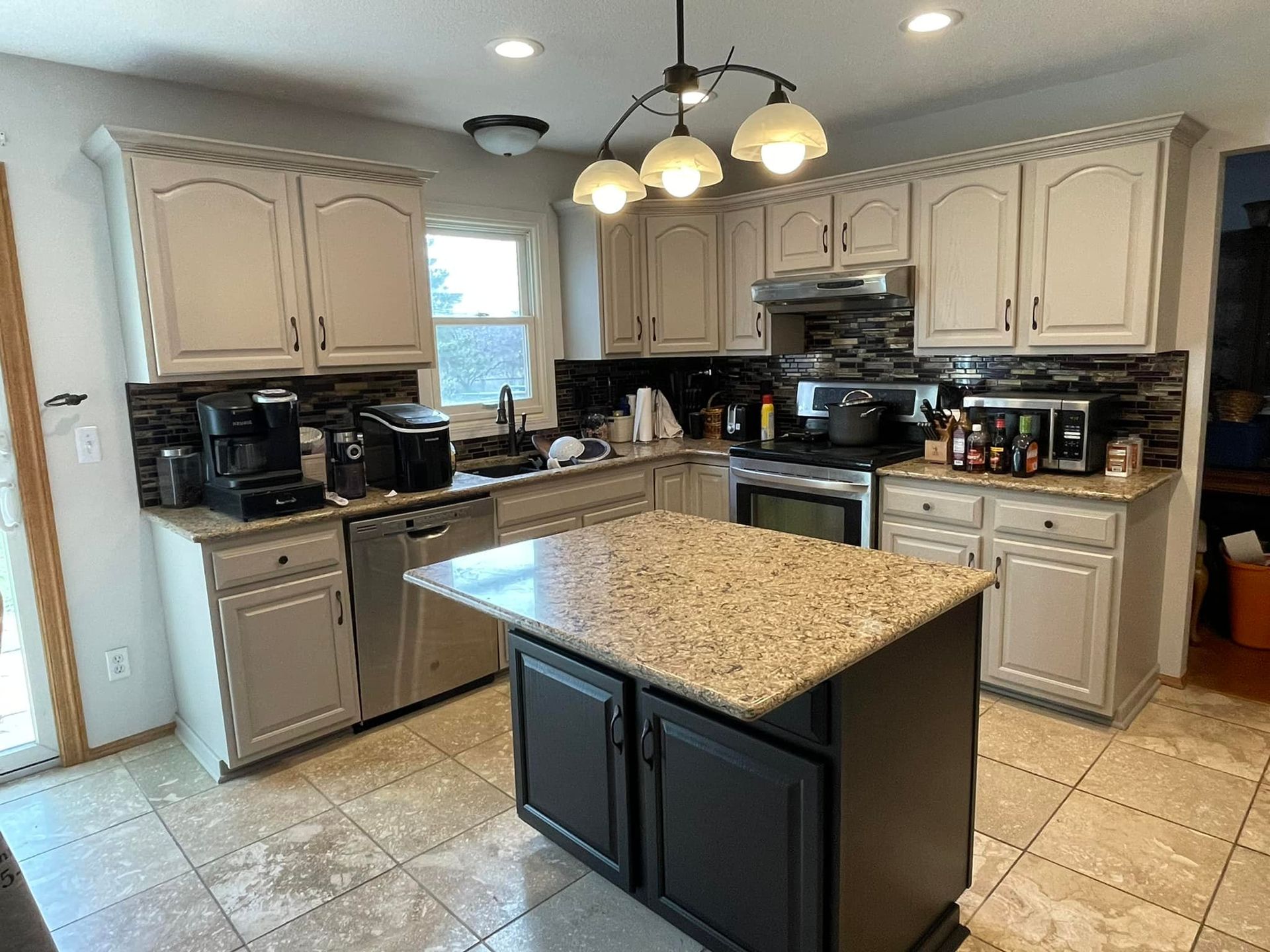 Kitchen with light beige cabinets, dark island, granite countertop, and appliances.