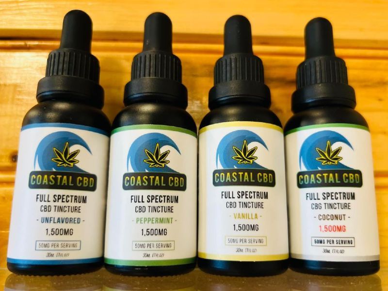 Four bottles of coastal cbd full spectrum cbd tincture are lined up on a wooden table.