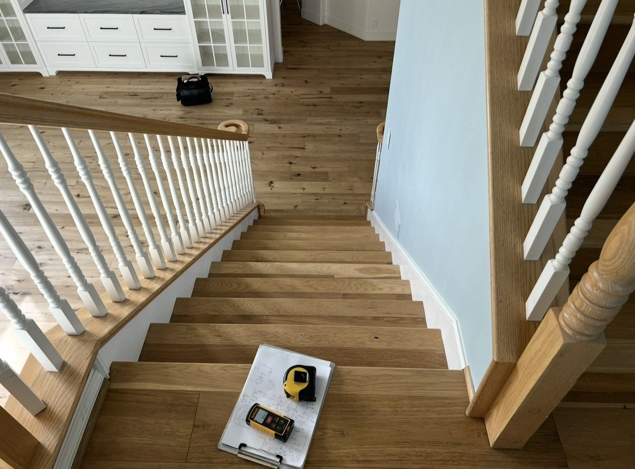 A wooden staircase with a white railing and a tape measure on the floor.