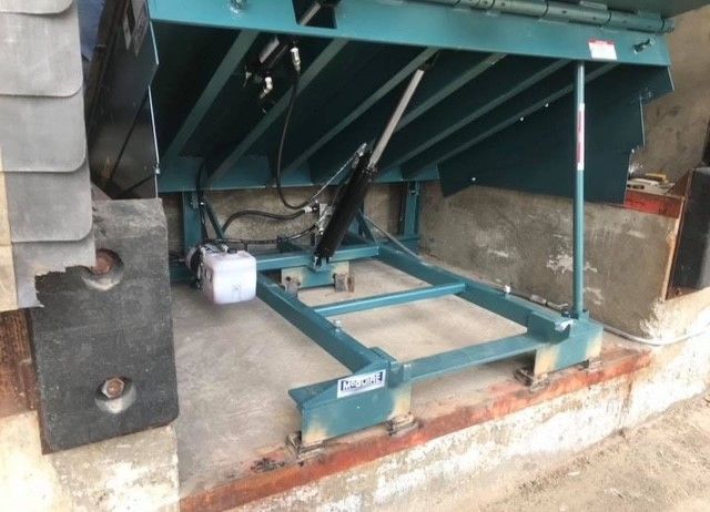 A blue machine is sitting on the ground next to a brick wall.