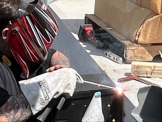 A man wearing a lincoln welding glove is welding a piece of metal