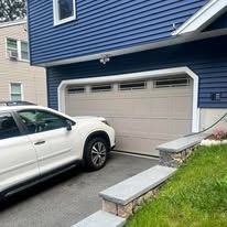 A white car is parked in front of a blue house with a garage door