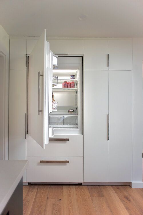 A kitchen with white cabinets and a refrigerator with the door open.