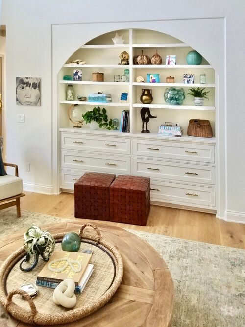 A living room with a table , chairs , shelves and ottomans.