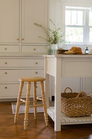 A wooden stool is sitting next to a white table in a kitchen.