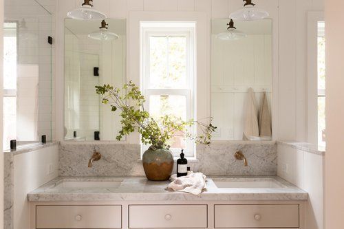 A bathroom with two sinks , two mirrors and a window.