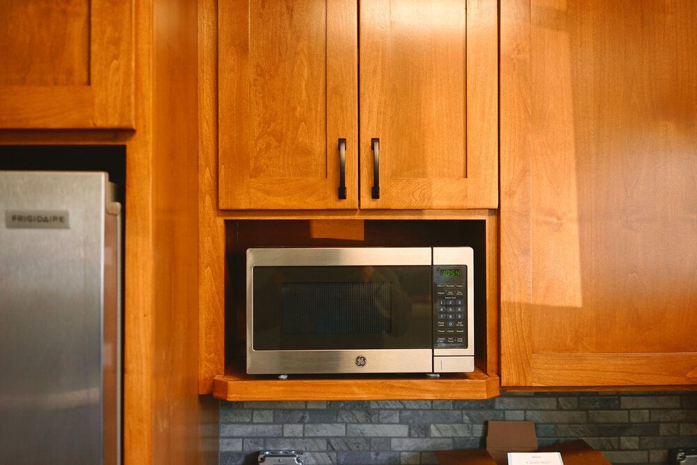 A microwave oven is sitting inside of a wooden cabinet in a kitchen.