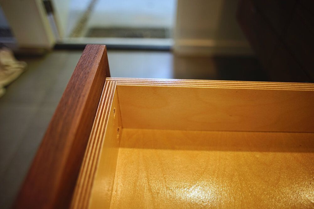 A close up of a wooden drawer with a door in the background.