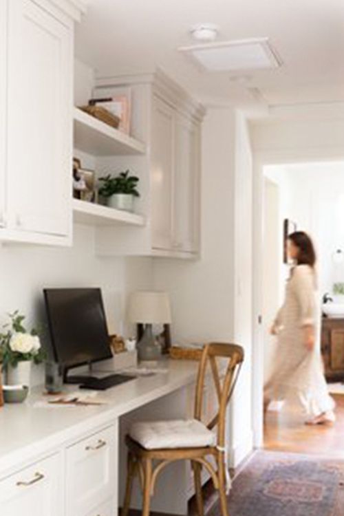A woman is walking past a desk with a computer on it.
