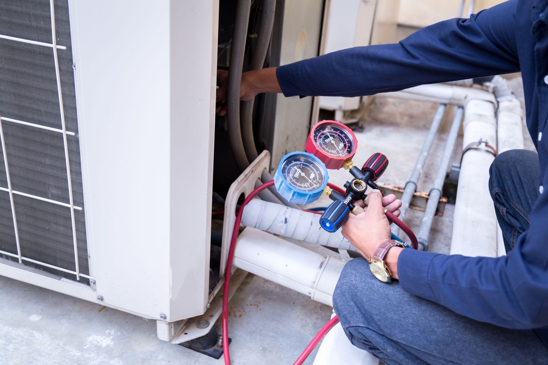 Person in overalls installing or repairing an air conditioner on a blue wall.