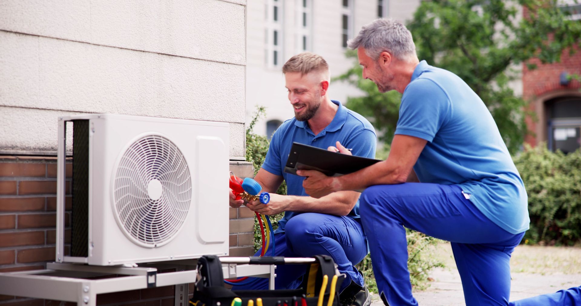 HVAC technician working on an outdoor air conditioning unit, using gauges and tools.