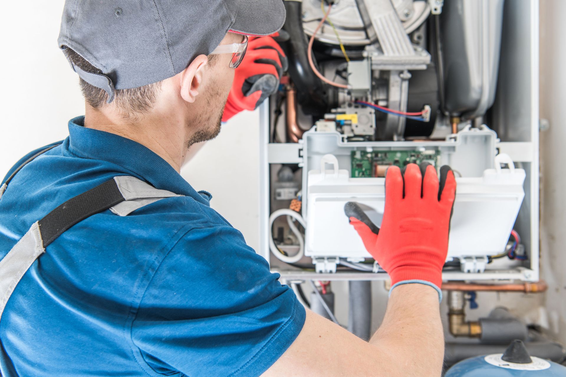A person wearing gloves and a cap working on a heating system.