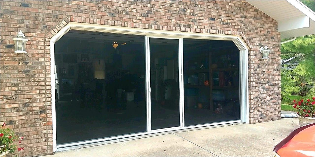 a car is parked in front of a brick garage with screened in garage doors