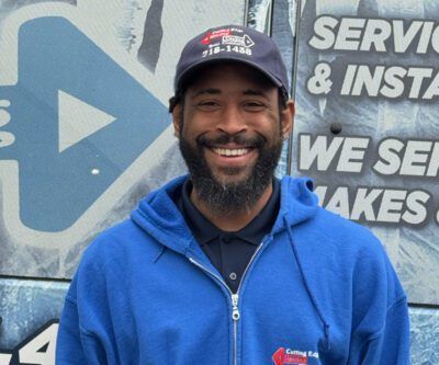 Smiling man in a blue hoodie and cap standing in front of a service and installation sign.