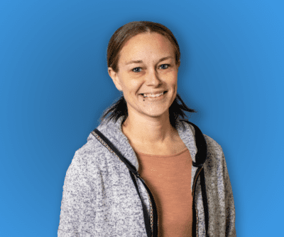 Smiling person in a gray hoodie over a rust shirt against a blue background